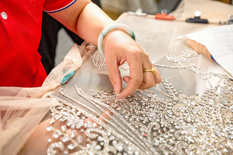 Eine Handwerkerin setzt von Hand Pailletten auf Tüll